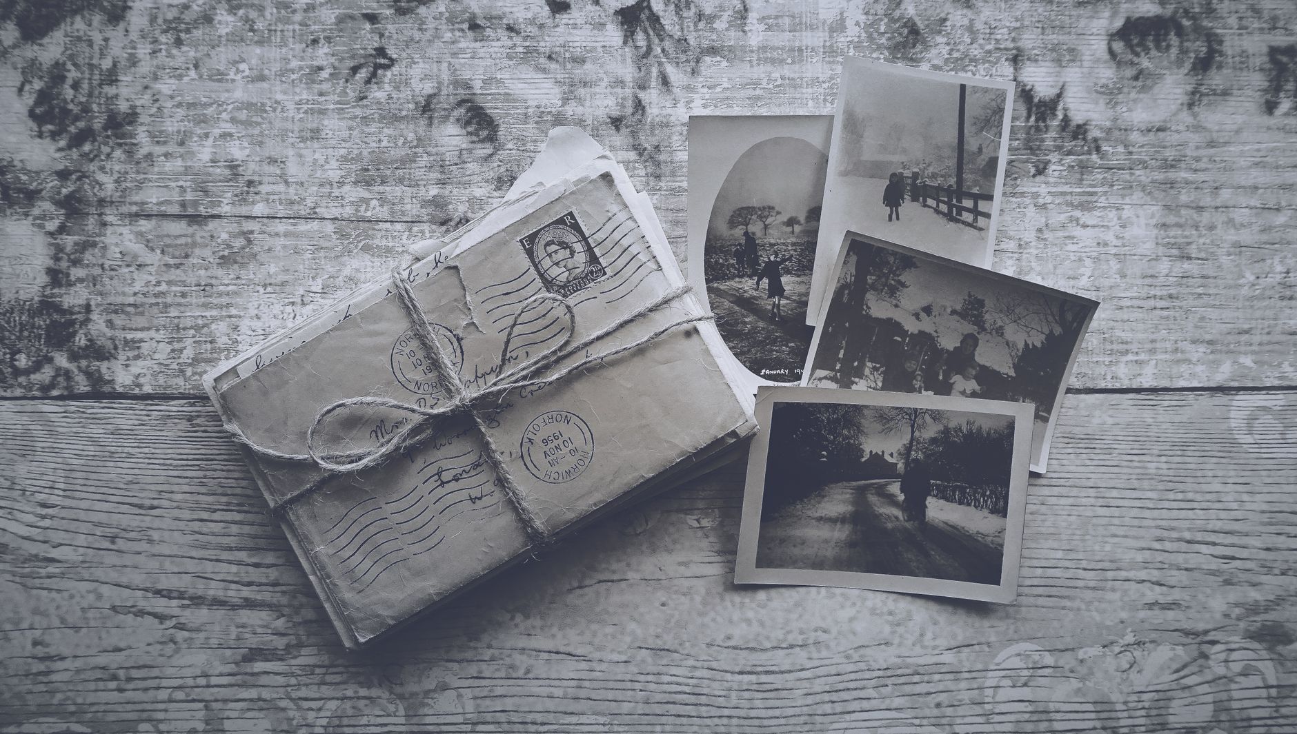 Flatlay of vintage letters tied with twine and black and white photos on a wooden surface.