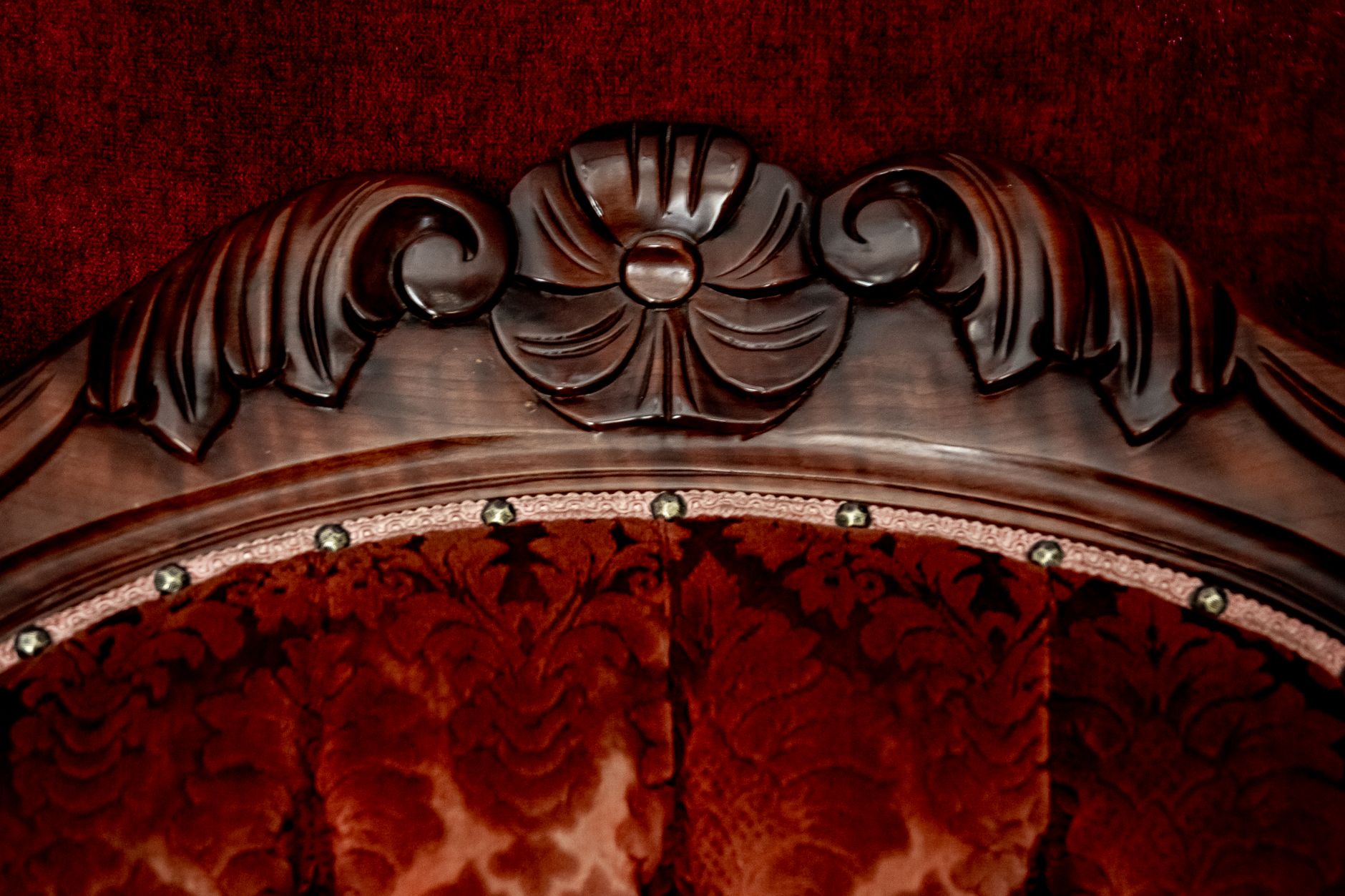 Close-up of ornate carved wood detail on vintage furniture with rich red velvet upholstery.