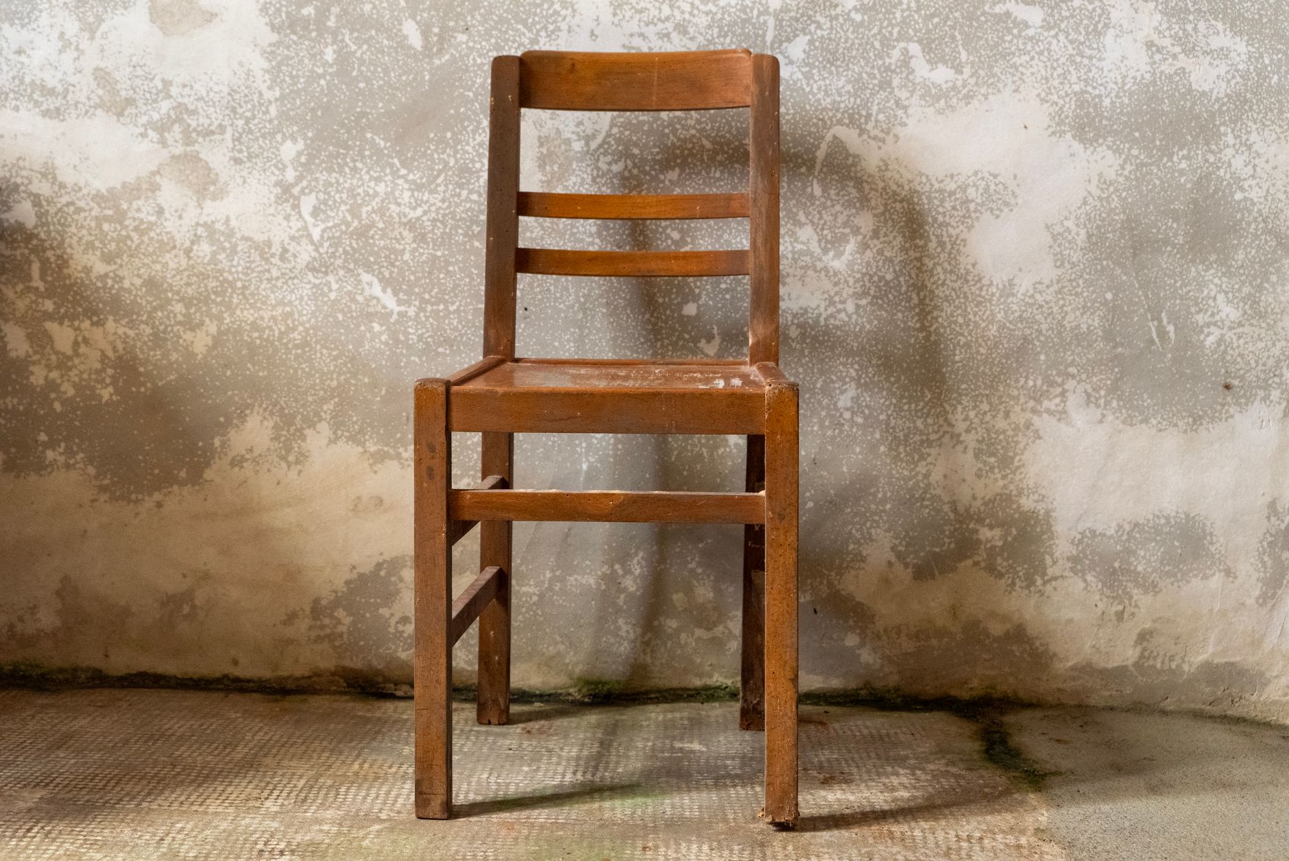 A single wooden chair placed against a rustic, textured wall in an indoor setting.