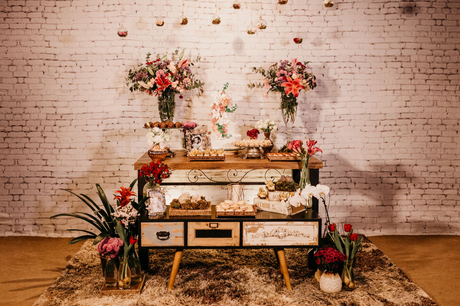 Assorted delicious sweets served on creative wooden cabinet on fluffy carpet decorated with bright fragrant flowers bouquets in light studio